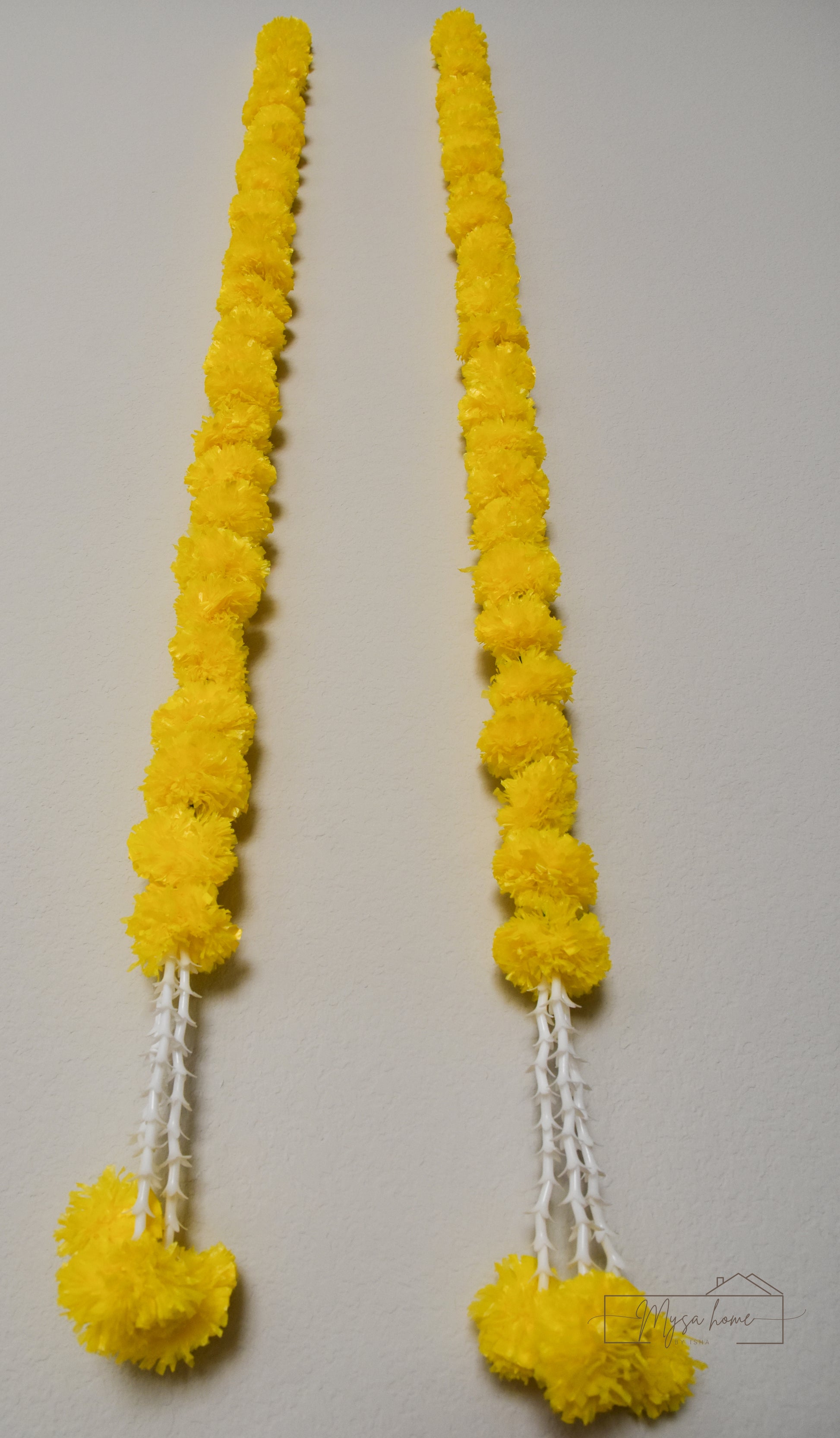 Two long yellow flower garlands with white string tassels, displayed vertically against a plain light background.