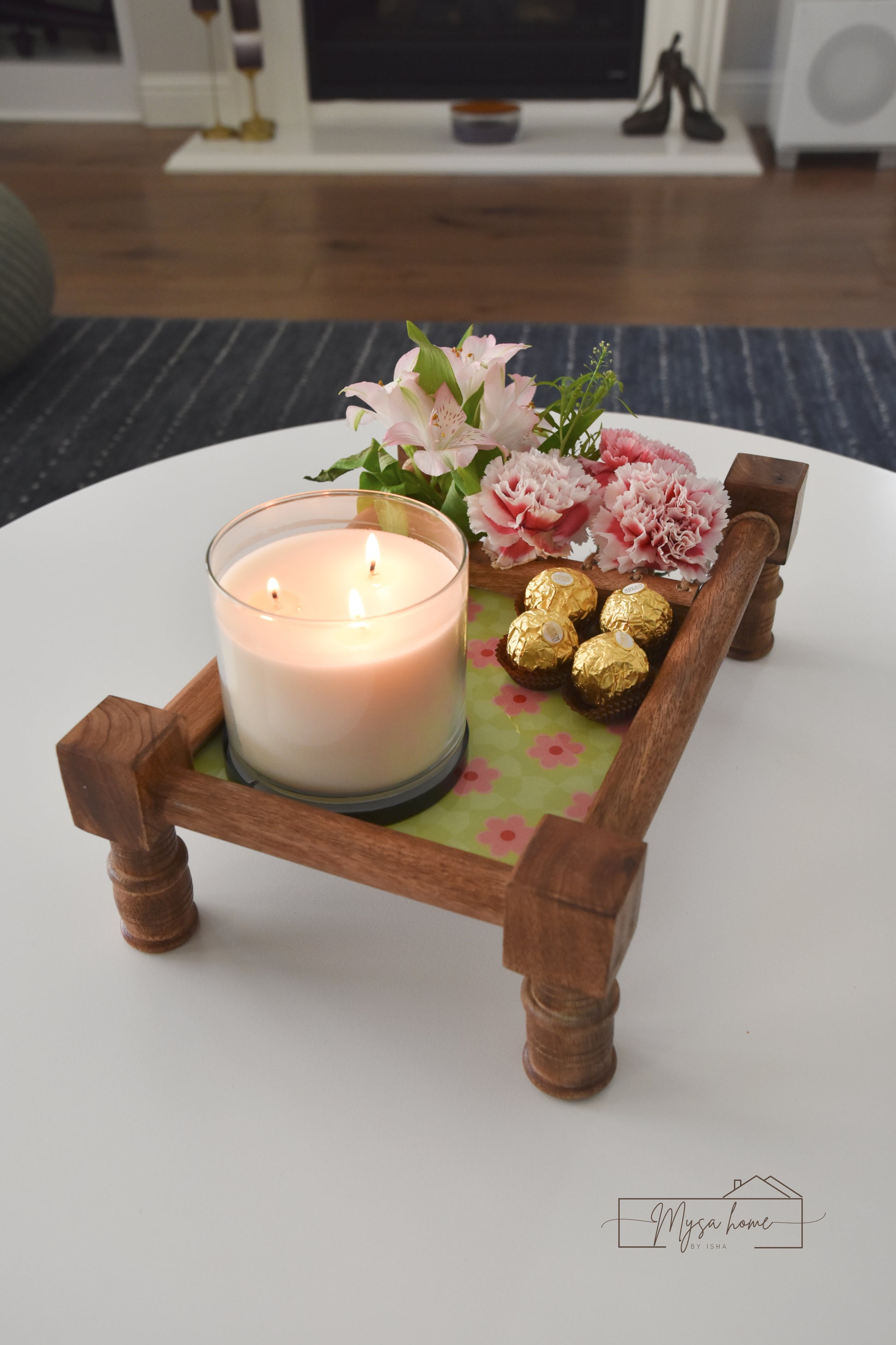 Candle on a wooden tray with flowers and chocolates on a table
