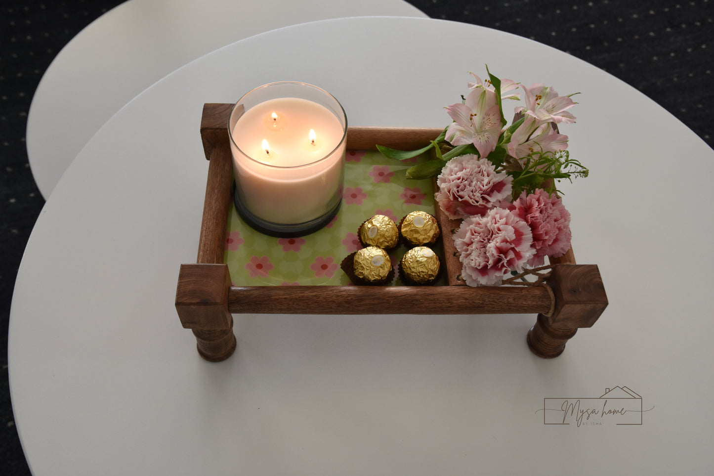 Decorative tray with a candle, flowers, and chocolates on a white surface.